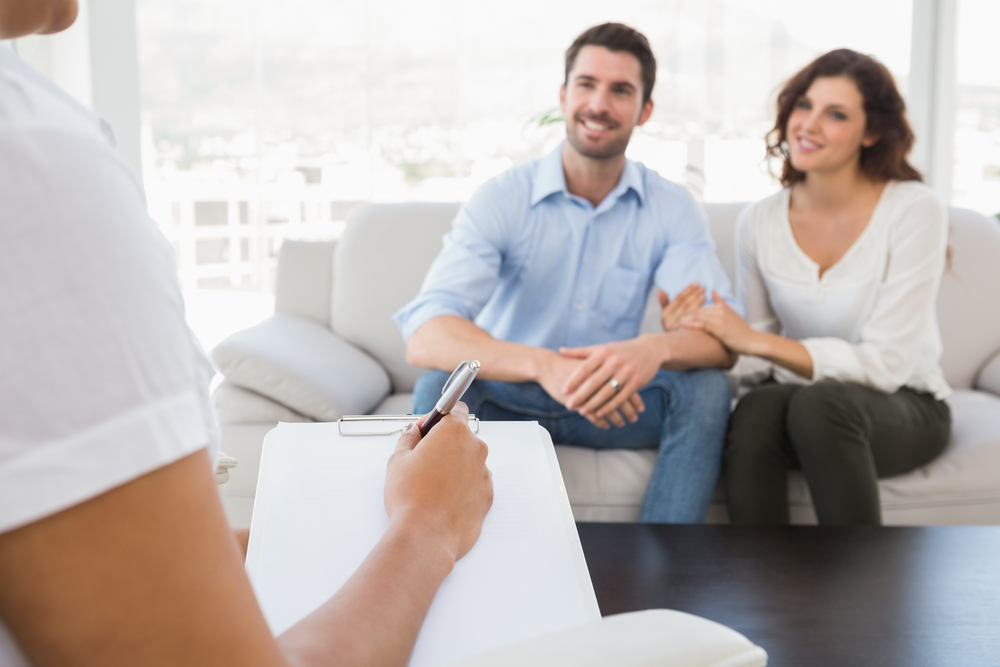 Reconciled couple smiling and talking with their therapist in the office