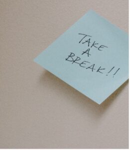 A blue sticky note on a beige surface with the handwritten message, TAKE A BREAK!!.
